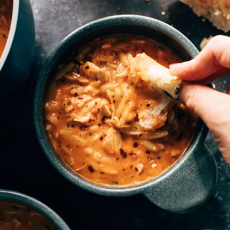 White hand dipping bread into soup