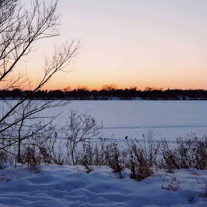 A winter scene with snow covering an empty field beneath a sky tinged with orange.
