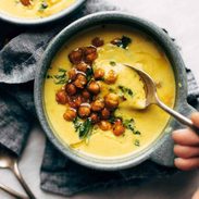 Two bowls of golden soup with roasted chickpeas and olive oil drizzled on top.