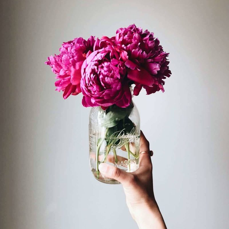 Person holding a jar with flowers.