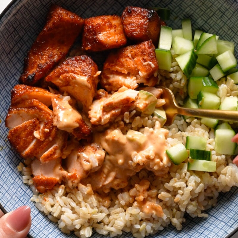 Air fryer salmon in a bowl with rice, cucumber, and sauce.