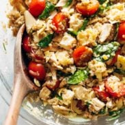 A quinoa chicken salad with tomatoes, and spinach in a glass bowl.