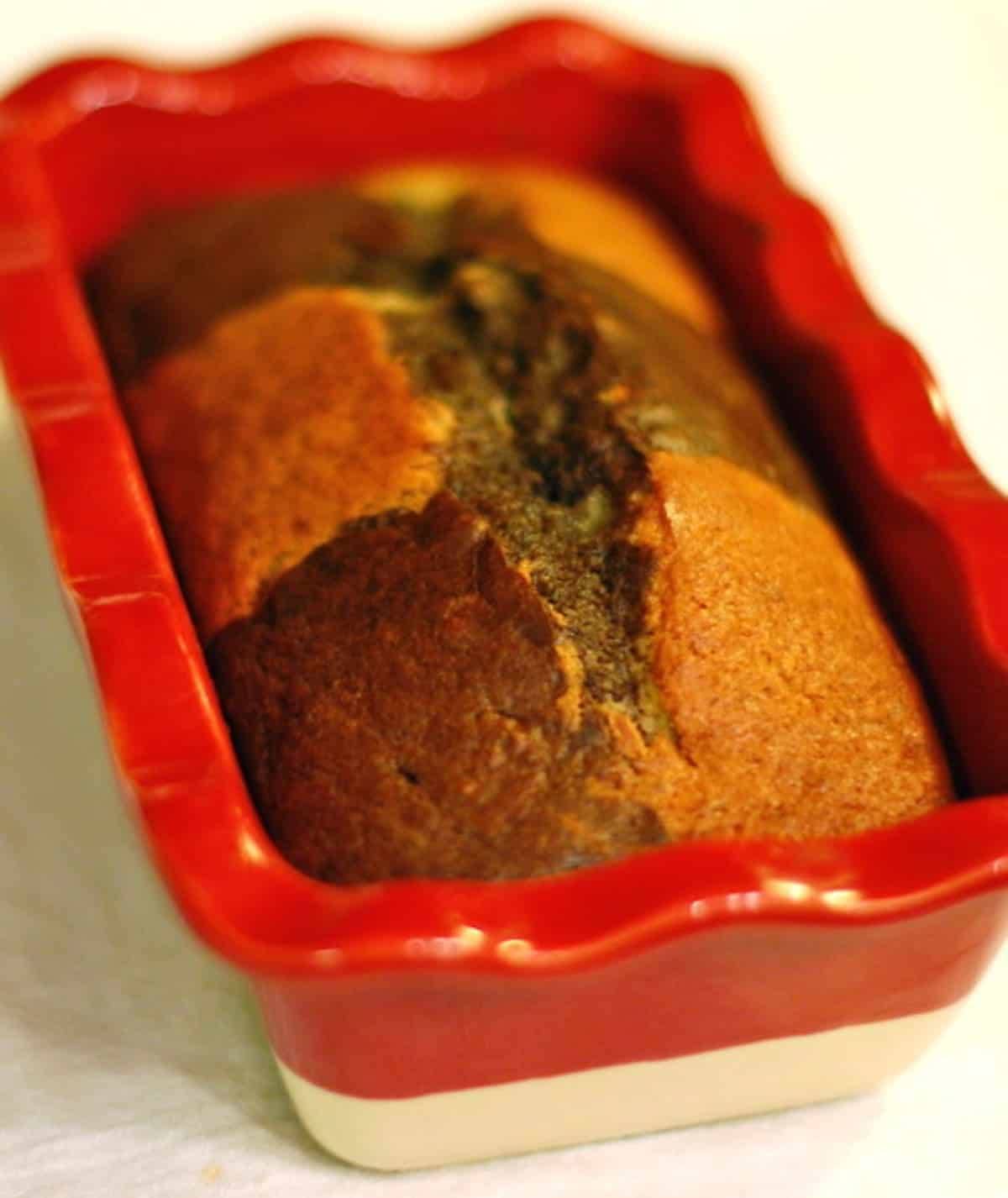 Loaf of chocolate checkered banana bread in a red baking dish.