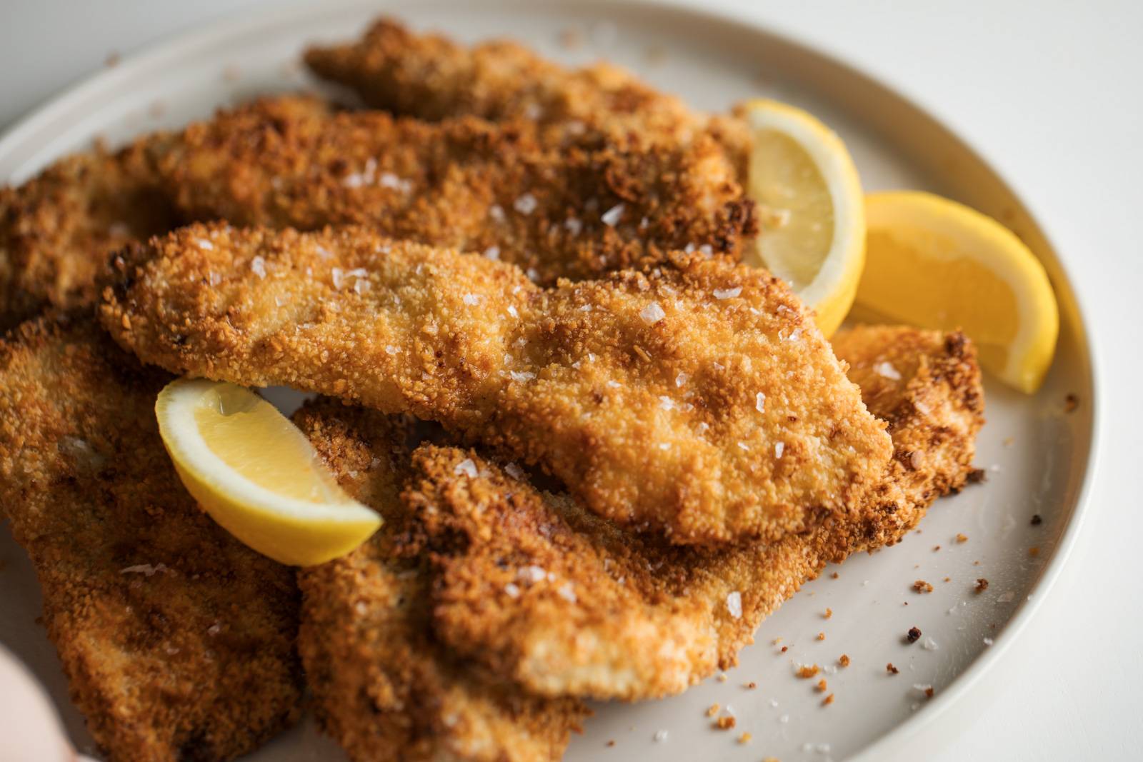 Crispy chicken cutlets on a plate with lemon wedges.
